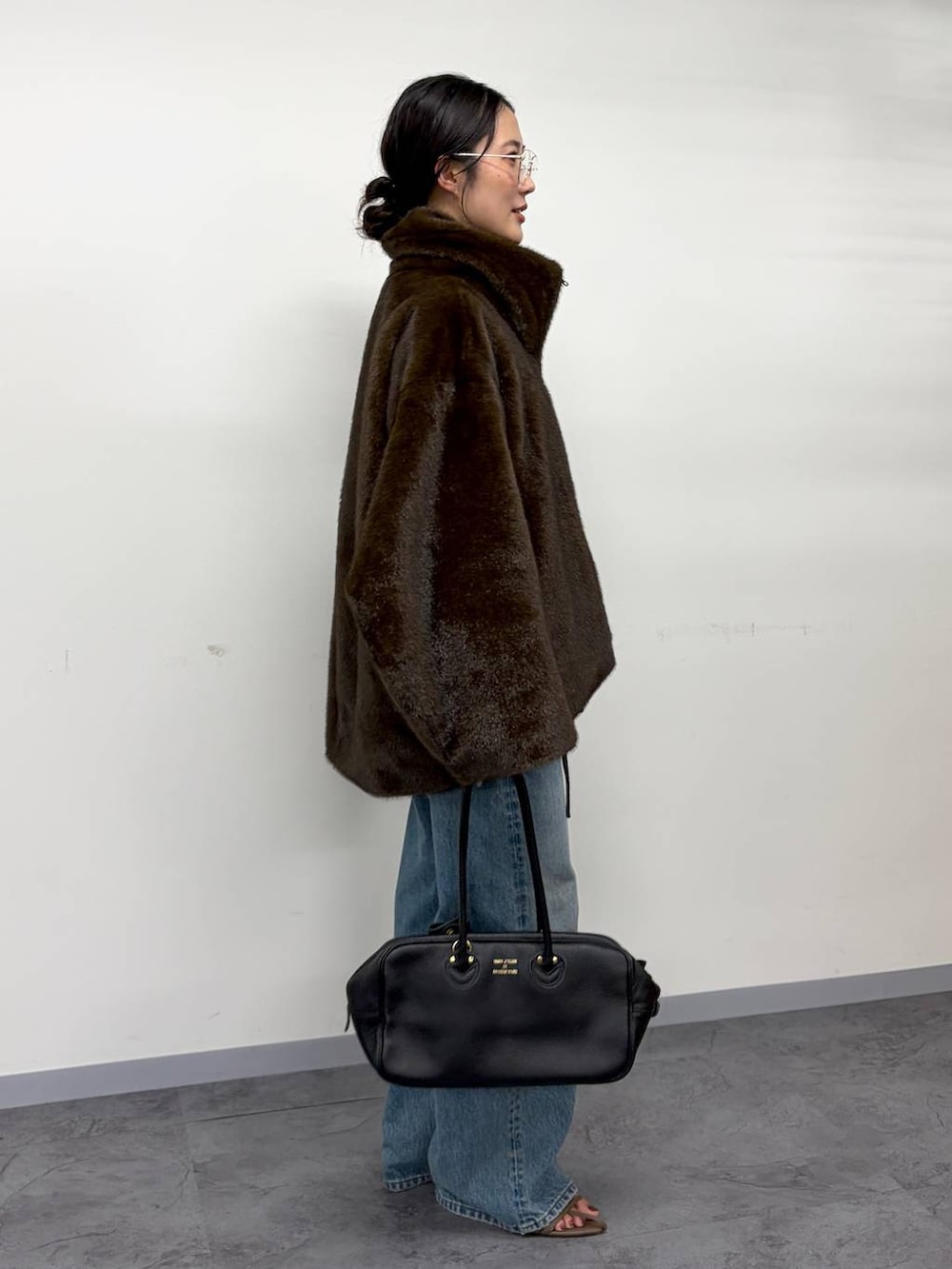 グレー系のニット/セーター、ブラウン系のムートンコート、ベージュ系のサンダルを着用したレディースの秋コーディネートの4枚目の写真