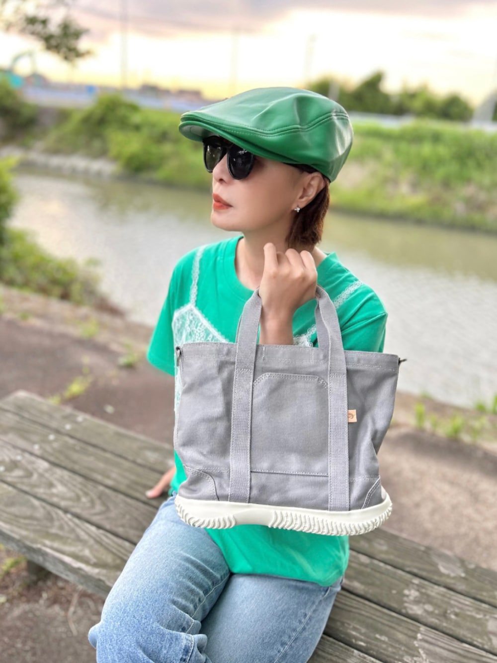 グレー系のトートバッグ、グリーン系のTシャツ/カットソー、ブルー系のデニムパンツを着用したレディースの春コーディネートの2枚目の写真