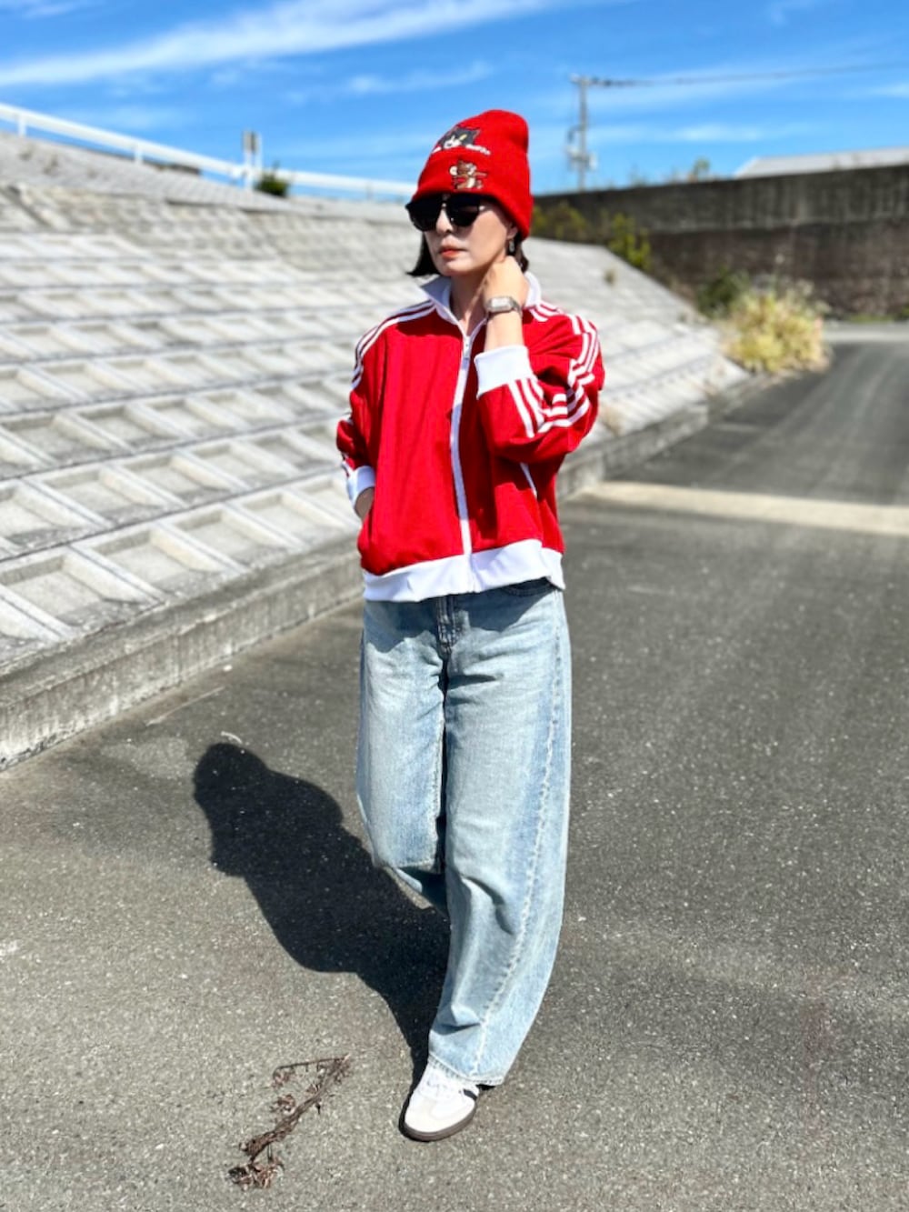 レッド系のジャージ、ブルー系のデニムパンツ、ホワイト系のスニーカーを着用したレディースの秋コーディネートの2枚目の写真