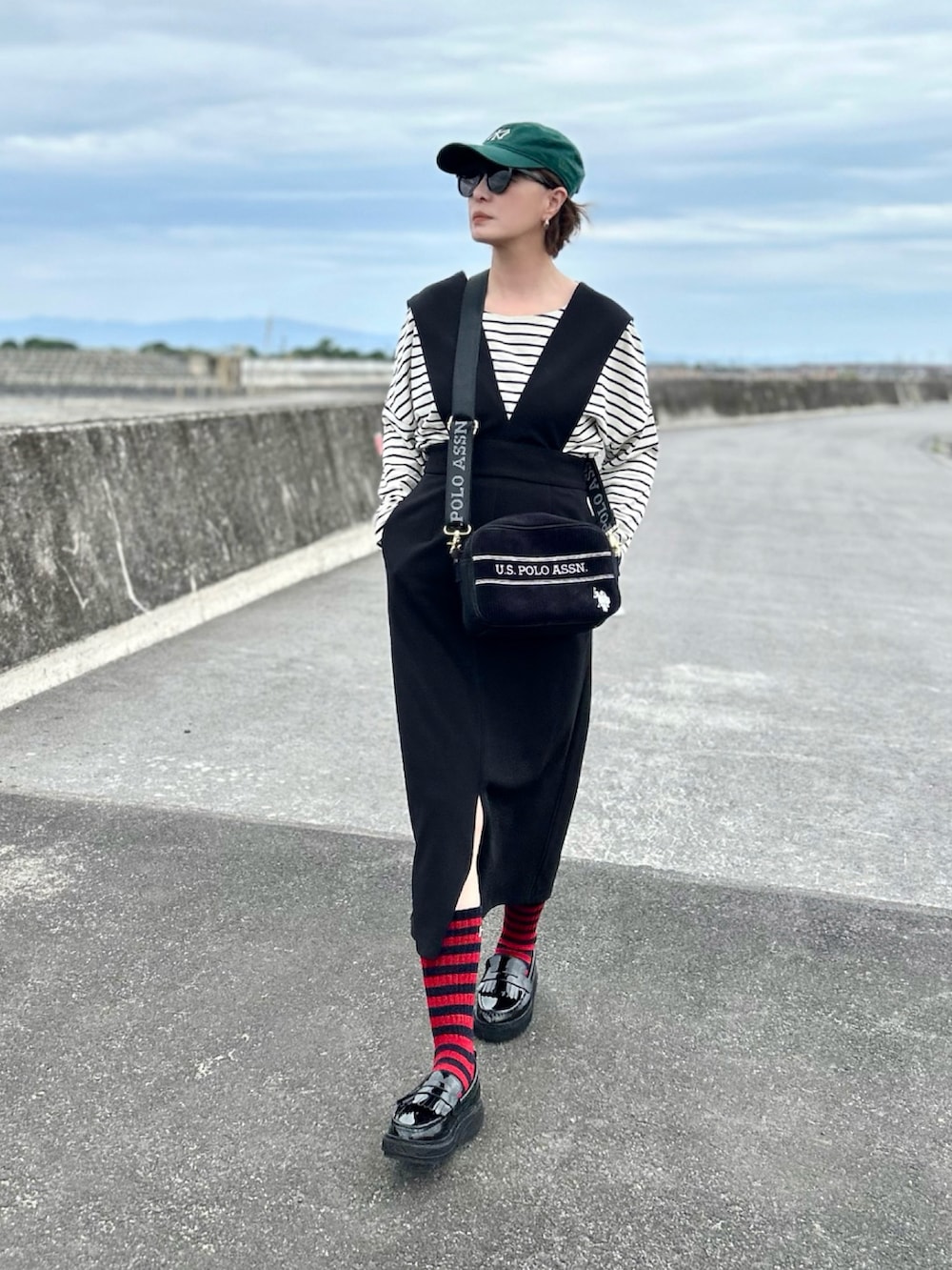 ブラック系のジャンパースカート、ホワイト系のTシャツ/カットソー、ブラック系のショルダーバッグを着用したレディースの春コーディネートの2枚目の写真