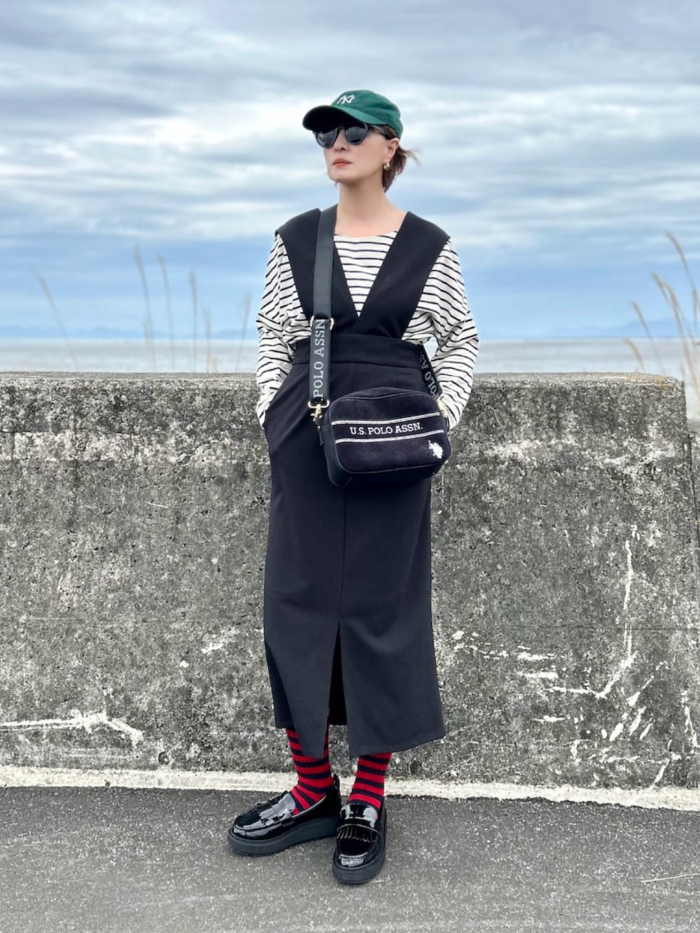 ブラック系のジャンパースカート、ホワイト系のTシャツ/カットソー、ブラック系のショルダーバッグを着用したレディースの春コーディネートの3枚目の写真