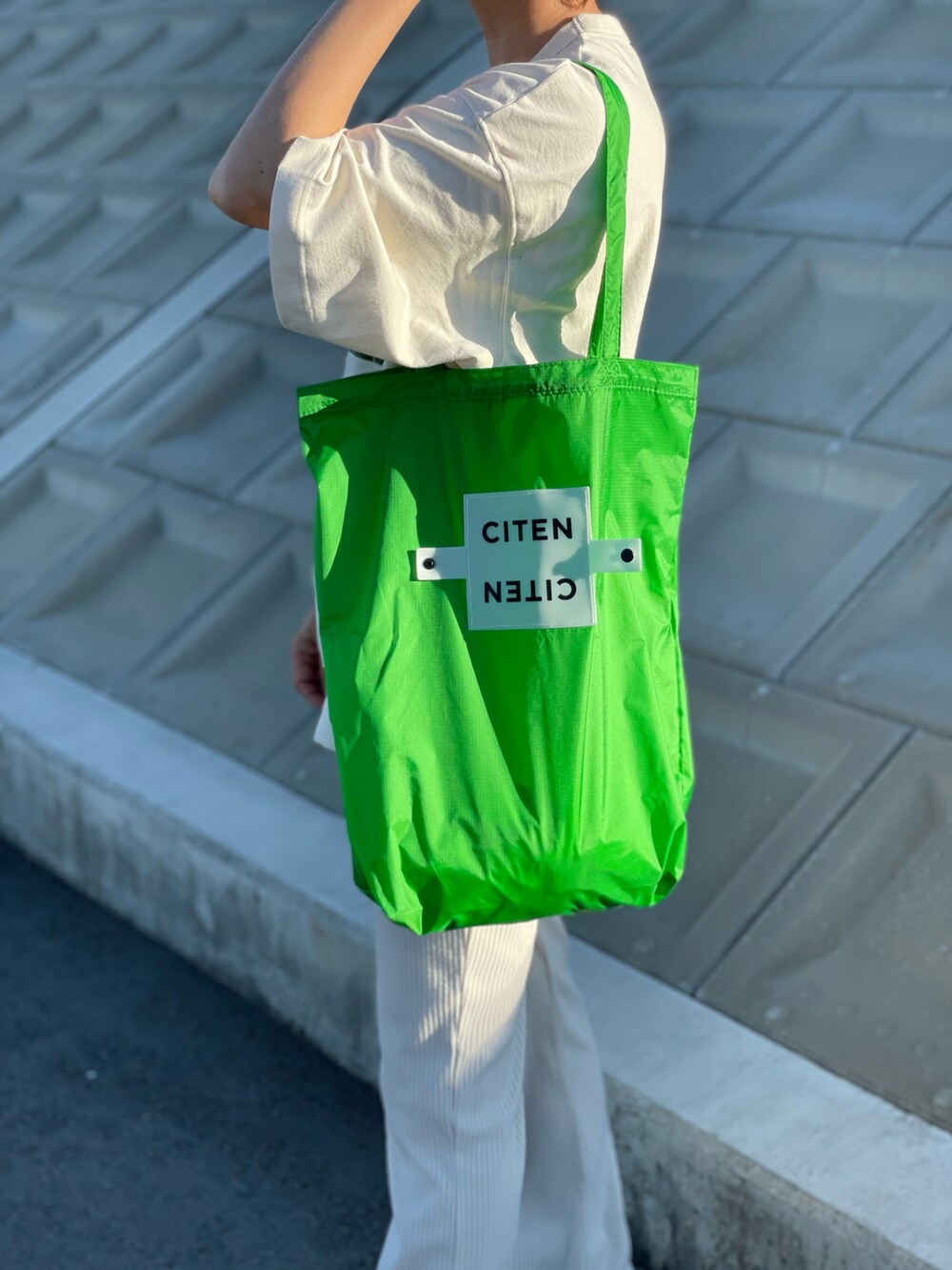 グリーン系のエコバッグ/サブバッグ、ホワイト系のトップス、ブラック系のスニーカーを着用したレディースの夏コーディネートの2枚目の写真