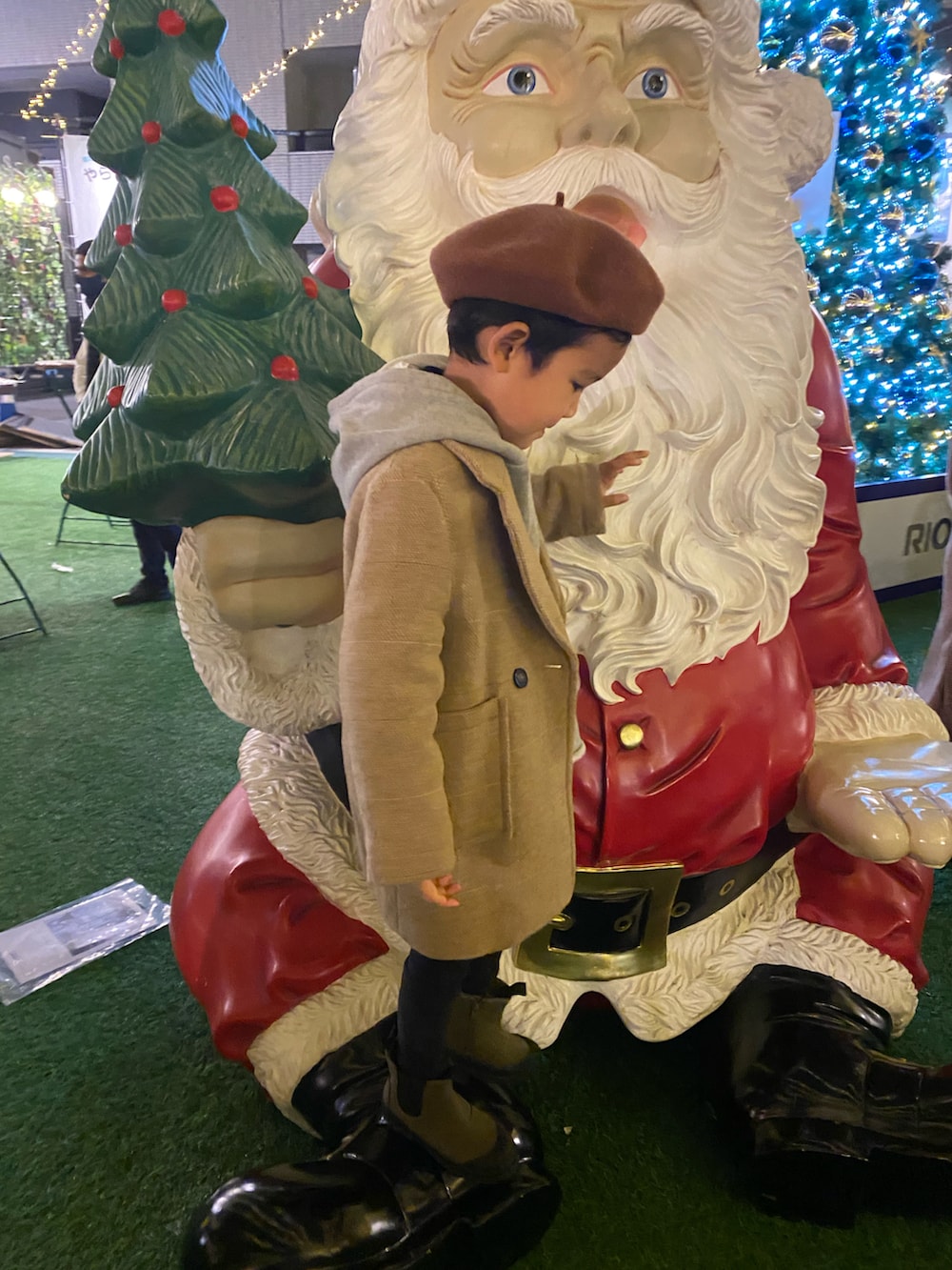 ベージュ系のチェスターコート、ブラック系のチノパンツ、グリーン系のブーツを着用したキッズの冬コーディネートの2枚目の写真