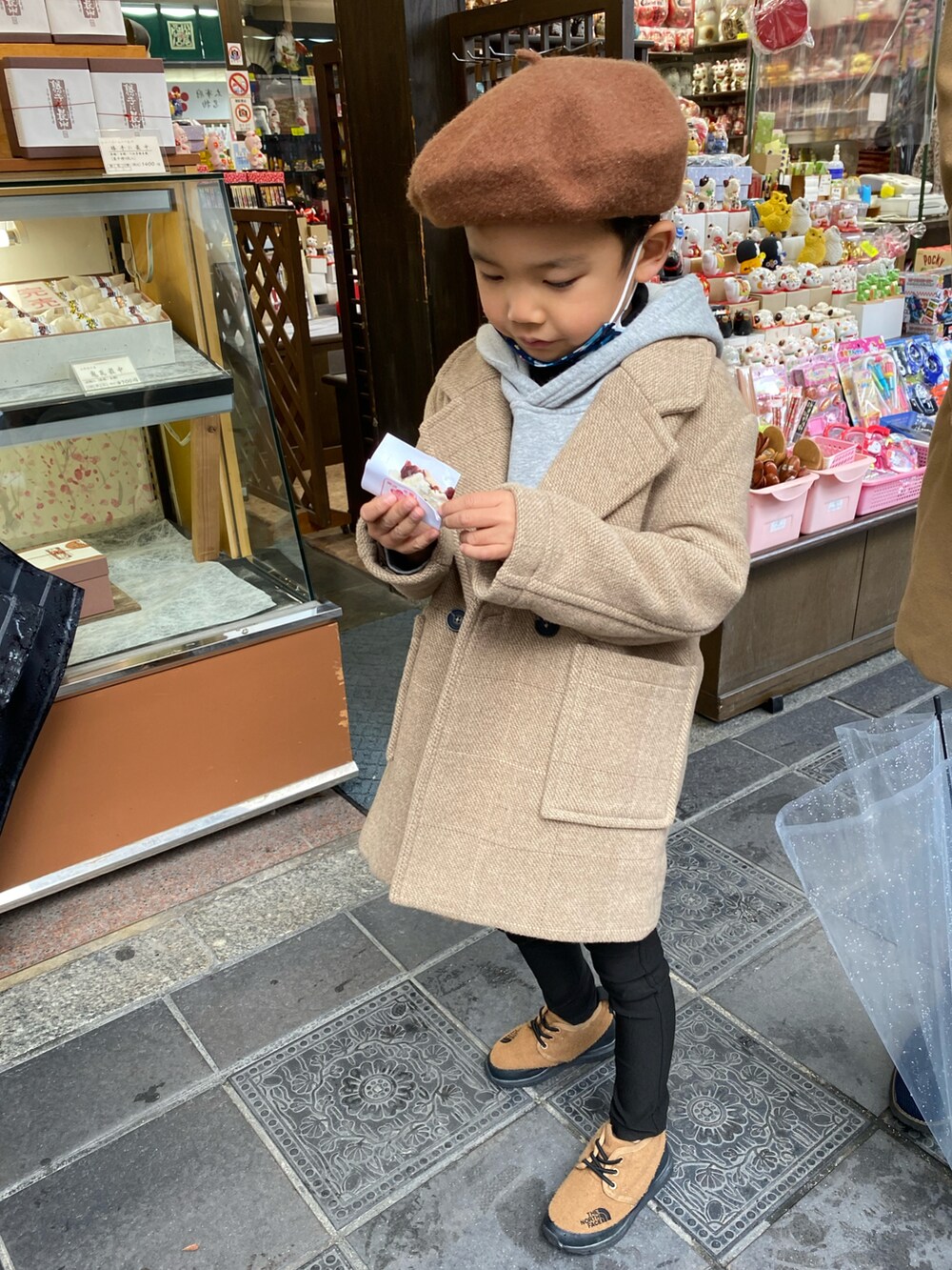 ベージュ系のチェスターコート、グレー系のパーカー、ブラック系のその他パンツを着用したキッズの秋コーディネートの2枚目の写真