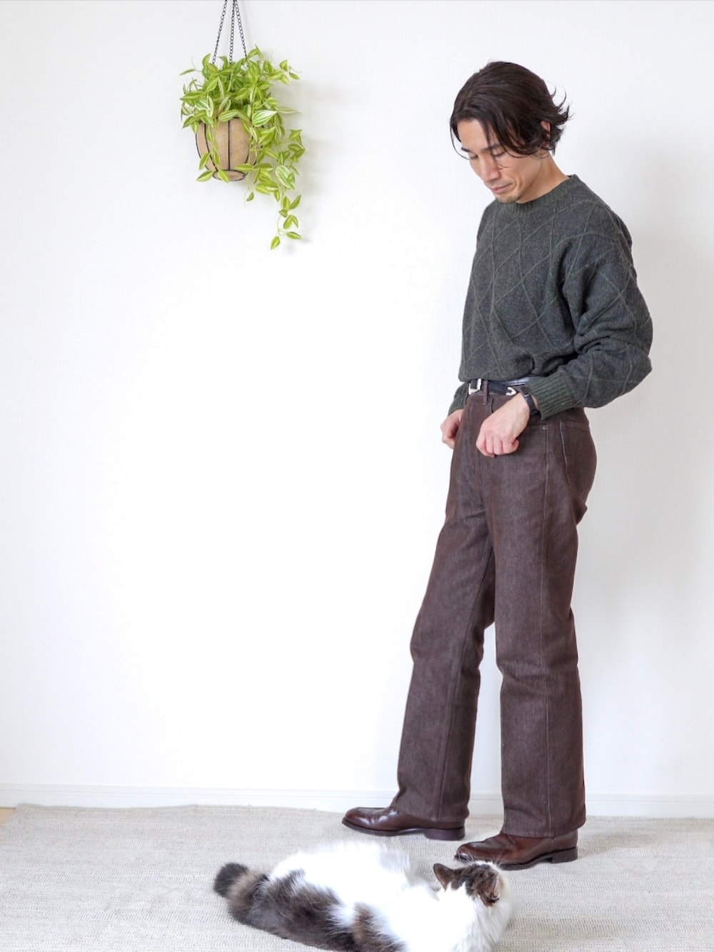 ブラウン系のデニムパンツ、ブラウン系のドレスシューズ、グリーン系のニット/セーターを着用したメンズの冬コーディネートの2枚目の写真