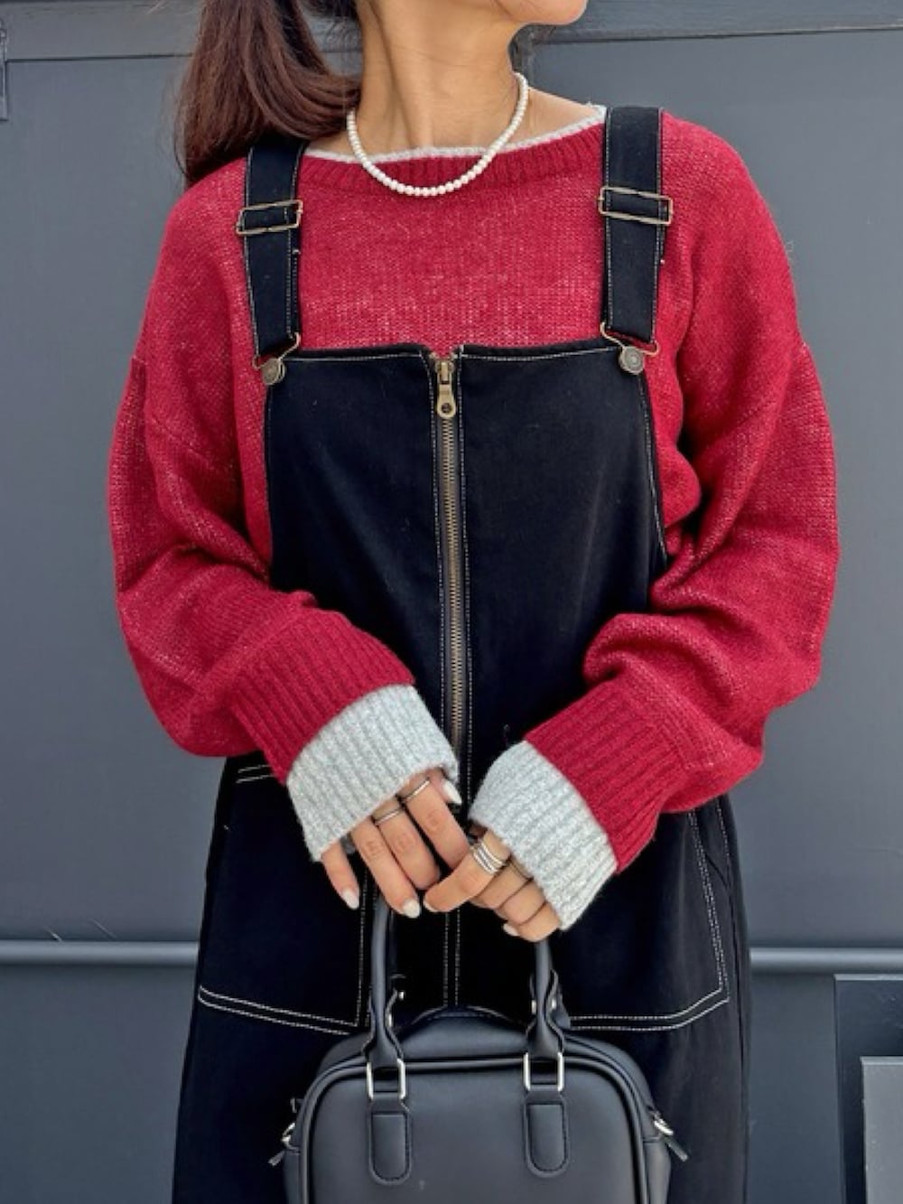 レッド系のニット/セーター、ブラック系のジャンパースカート、ブラック系のスニーカーを着用したレディースの秋コーディネートの2枚目の写真