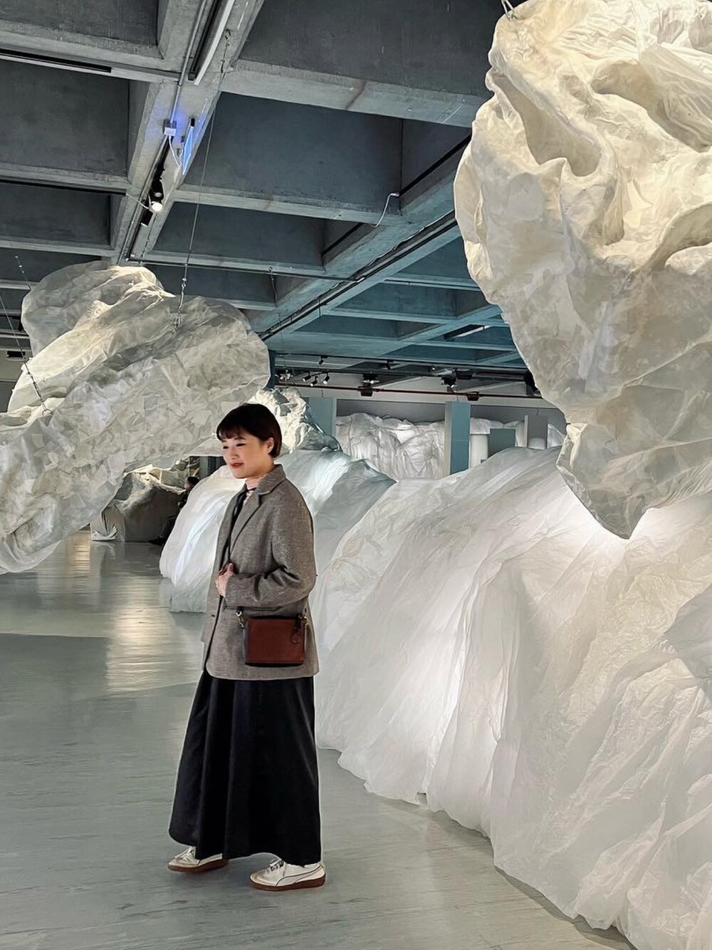 ベージュ系のチェスターコート、ブラック系のワンピース、ホワイト系のスニーカーを着用したレディースの冬コーディネートの2枚目の写真