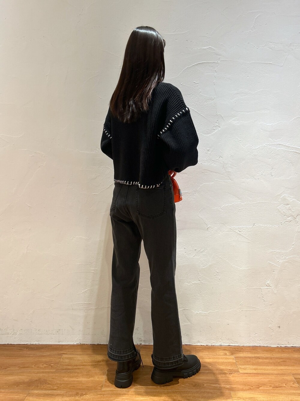ブラック系のニット/セーター、ブラック系のデニムパンツ、オレンジ系のショルダーバッグを着用したレディースの冬コーディネートの2枚目の写真
