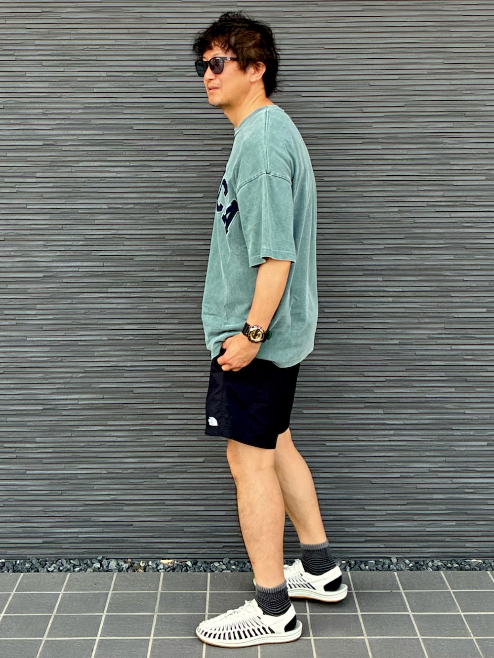 グリーン系のTシャツ/カットソー、ブラック系のその他パンツ、ホワイト系のサンダルを着用したメンズの夏コーディネートの2枚目の写真