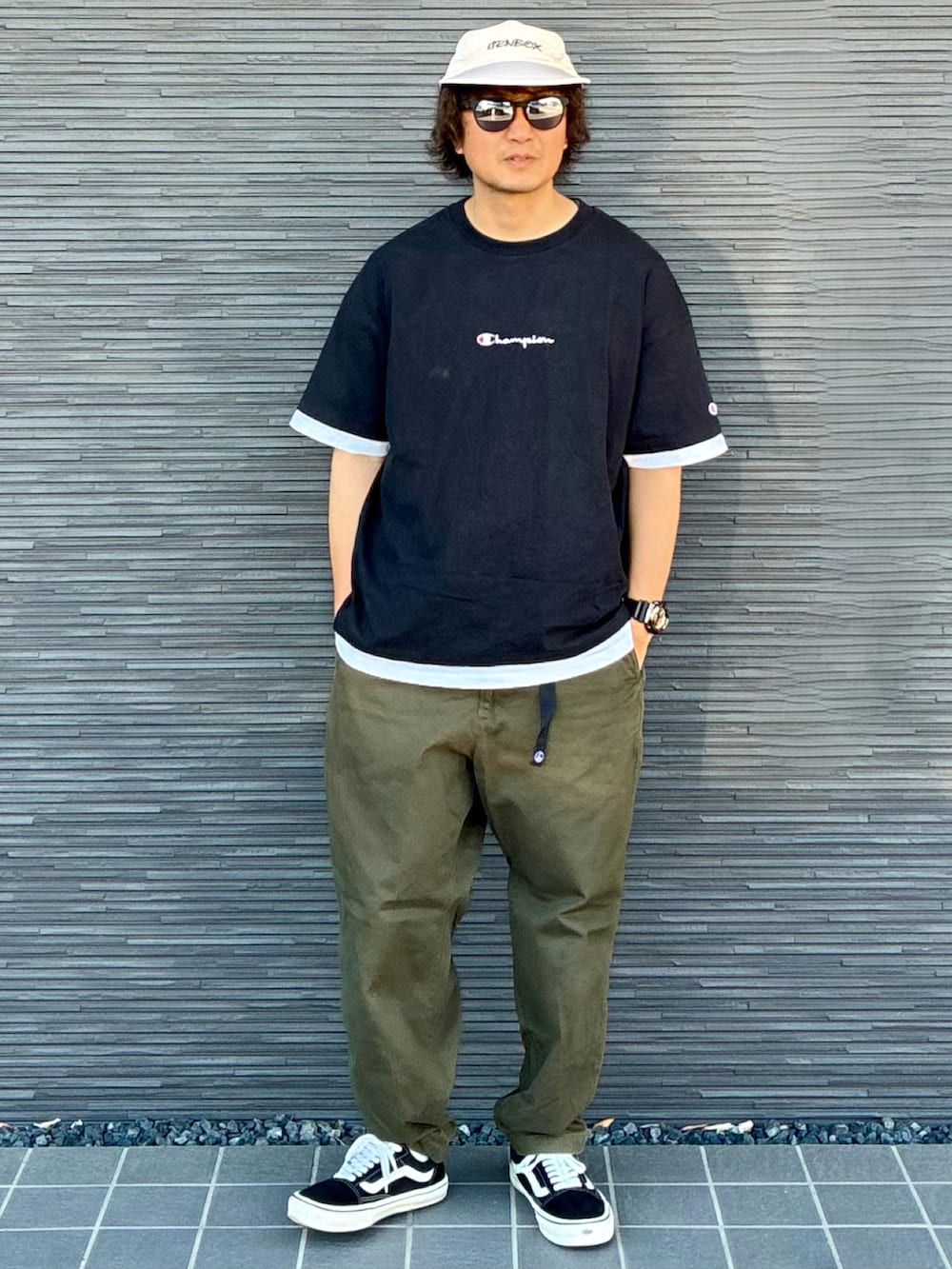 グリーン系のチノパンツ、ブラック系のスニーカー、ブラック系のTシャツ/カットソーを着用したメンズの夏コーディネートの2枚目の写真