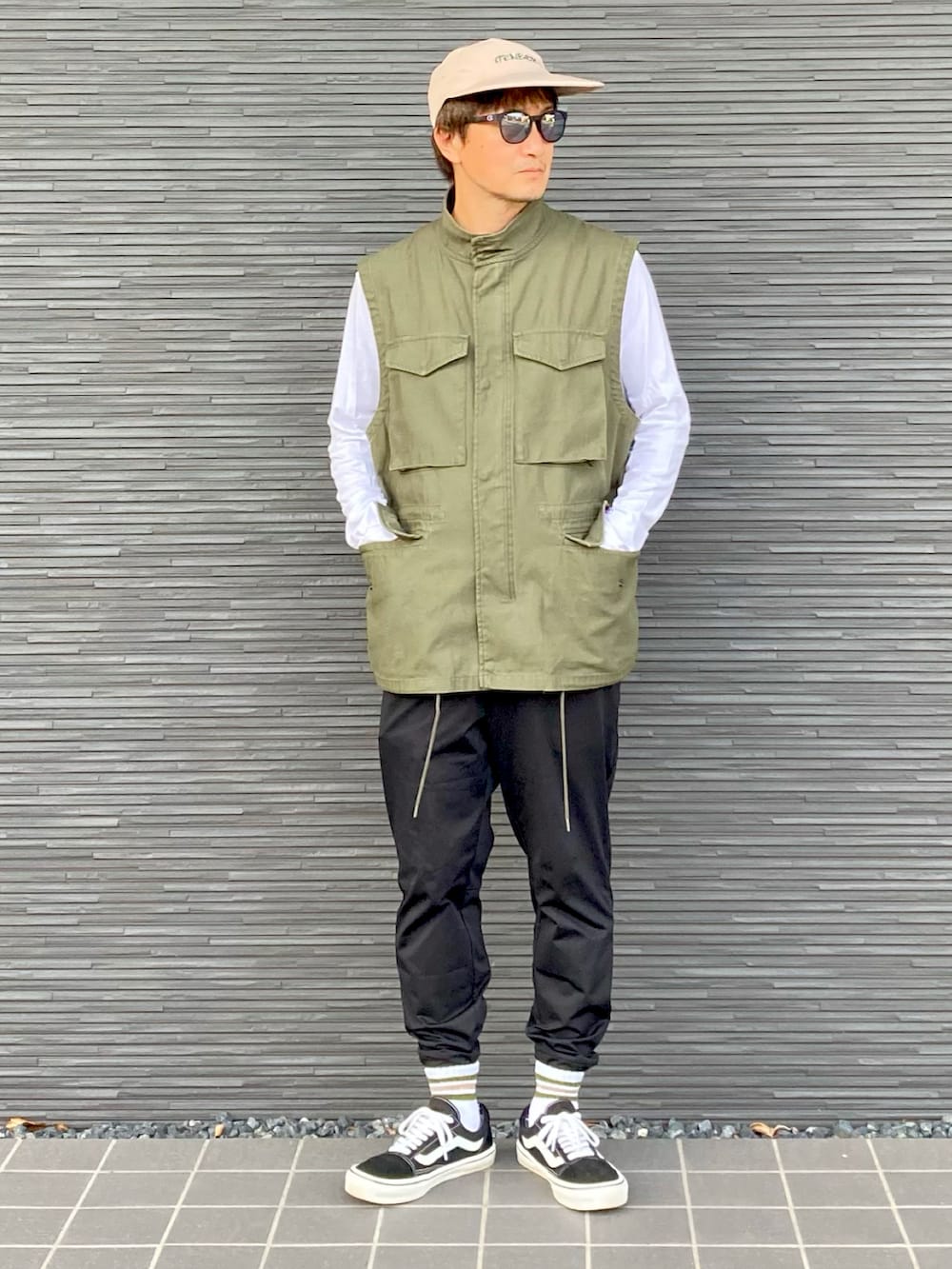 グリーン系のベスト、ホワイト系のTシャツ/カットソー、ブラック系のパンツを着用したメンズの秋コーディネートの2枚目の写真