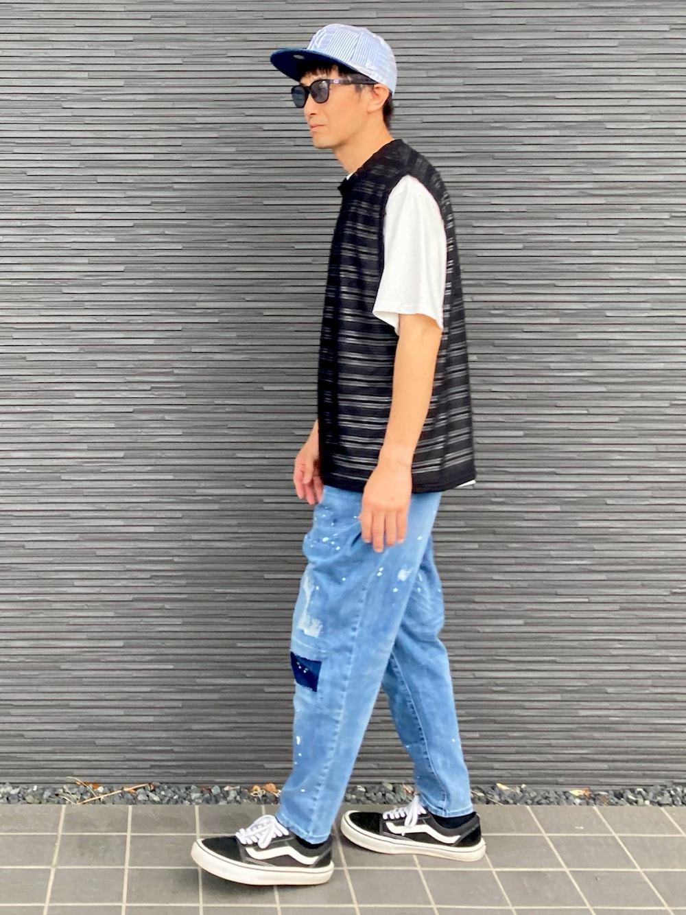 ブラック系のベスト、ブルー系のデニムパンツ、ブラック系のスニーカーを着用したメンズの夏コーディネートの3枚目の写真