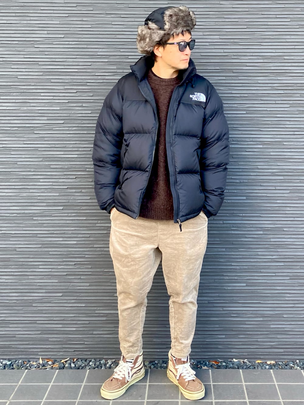 ブラック系のダウンジャケット/コート、ブラウン系のニット/セーター、ベージュ系のその他パンツを着用したメンズの冬コーディネートの2枚目の写真