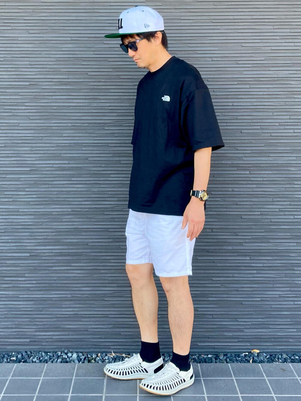 ブラック系のTシャツ/カットソー、ホワイト系のサンダル、ホワイト系のパンツを着用したメンズの夏コーディネートの2枚目の写真