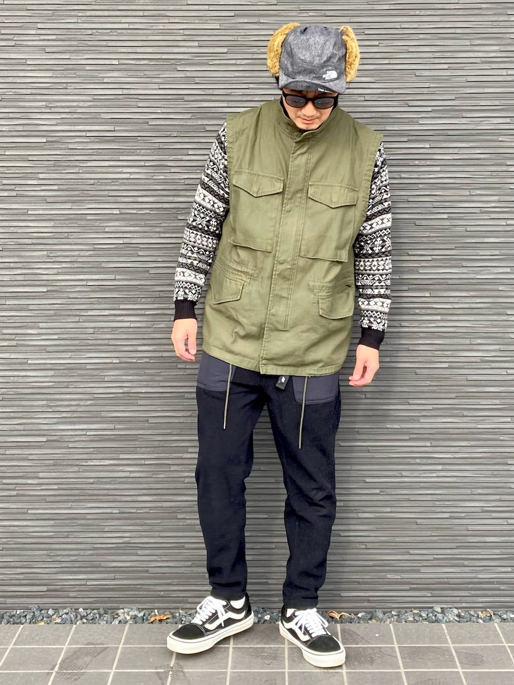 グリーン系のベスト、ブラック系のニット/セーター、ブラック系のパンツを着用したメンズの冬コーディネートの2枚目の写真