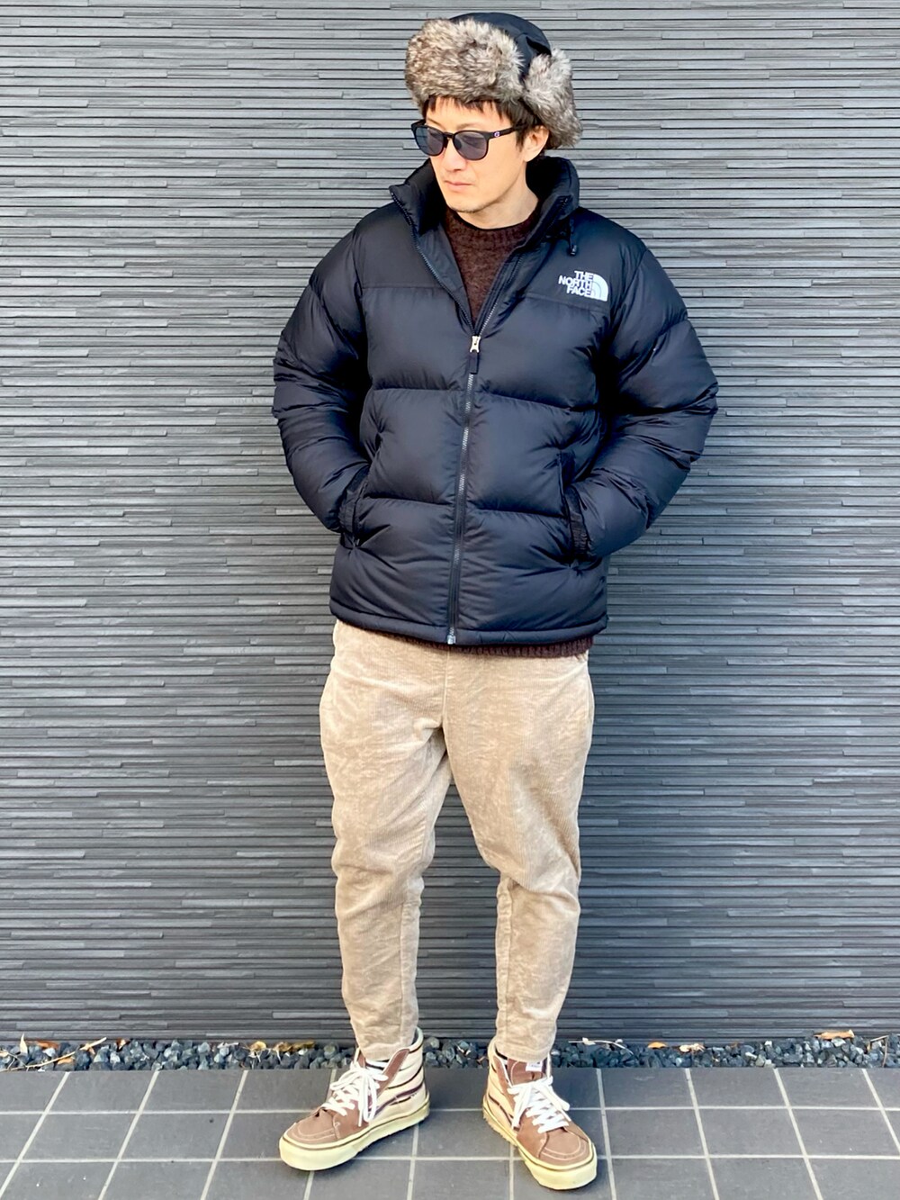 ブラック系のダウンジャケット/コート、ブラウン系のニット/セーター、ベージュ系のその他パンツを着用したメンズの冬コーディネートの5枚目の写真