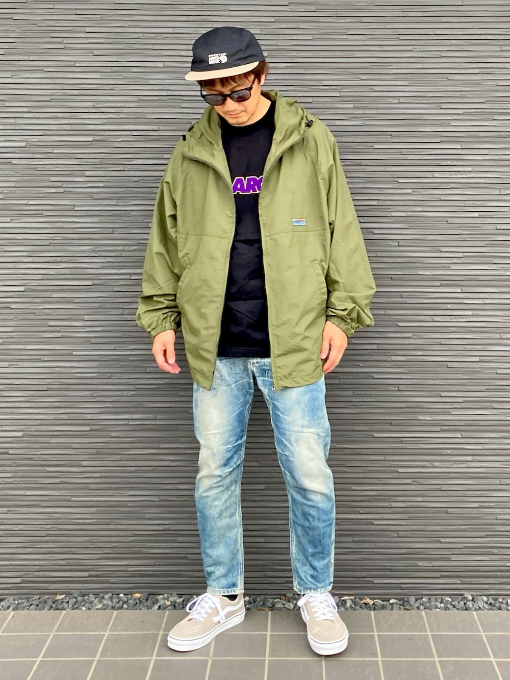 グリーン系のナイロンジャケット、ブラック系のTシャツ/カットソー、ブルー系のデニムパンツを着用したメンズの秋コーディネートの2枚目の写真