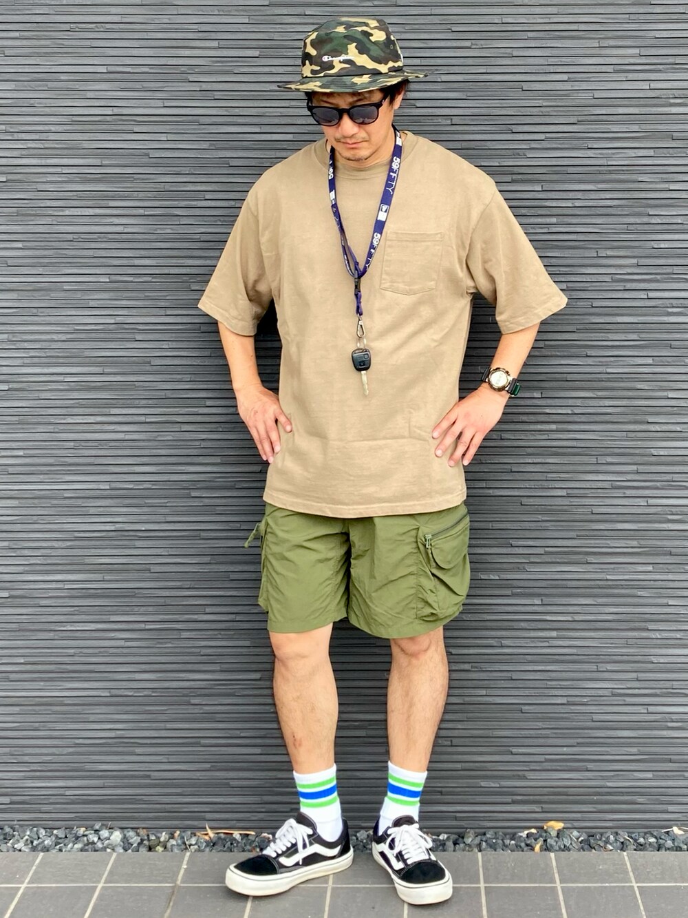 ブラック系のスニーカー、ベージュ系のTシャツ/カットソー、グリーン系のカーゴパンツを着用したメンズの夏コーディネートの2枚目の写真