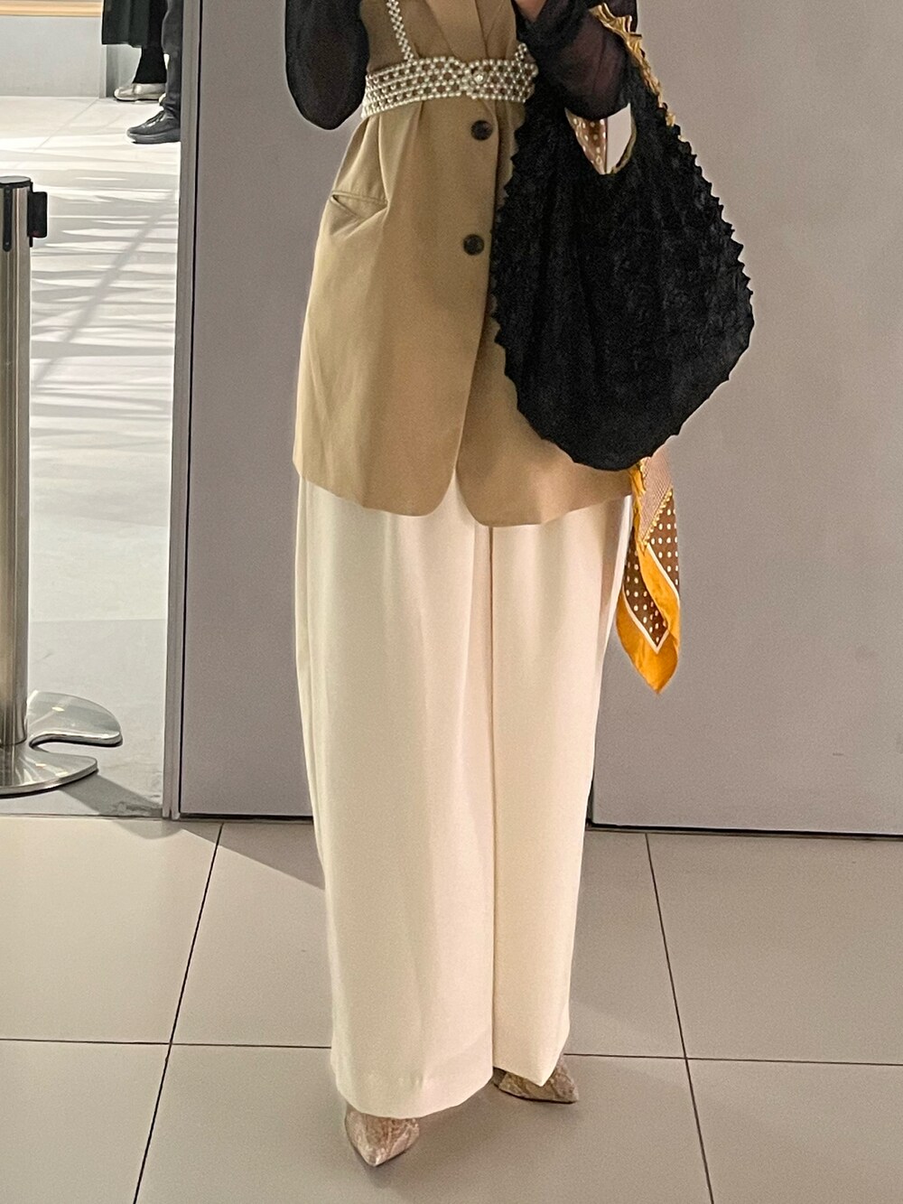 ベージュ系のベスト、ブラック系のハンドバッグ、ホワイト系のパンツを着用したレディースの春コーディネートの2枚目の写真
