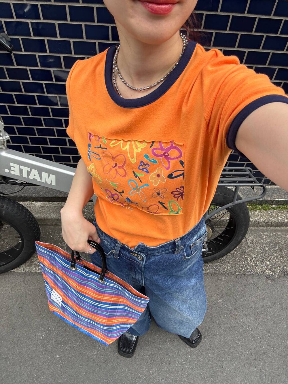 ブラック系のローファー、オレンジ系のTシャツ/カットソー、ブルー系のデニムパンツを着用したレディースの夏コーディネートの6枚目の写真