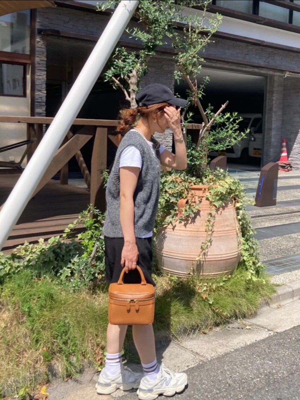 ホワイト系のスニーカー、ブラウン系のハンドバッグ、グレー系のベストを着用したレディースの夏コーディネートの2枚目の写真