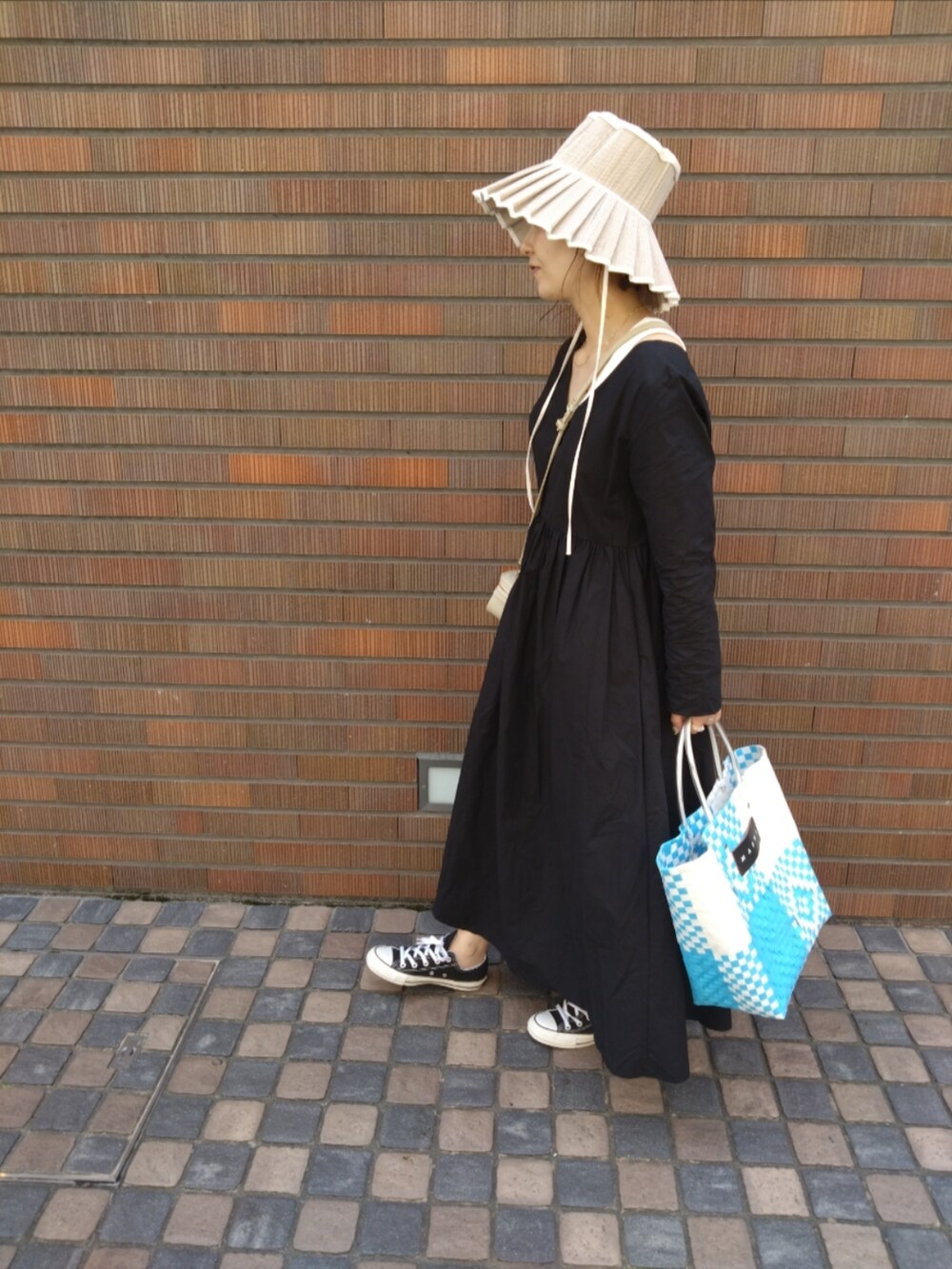 ブルー系のかごバッグ、ブラック系のスニーカー、ホワイト系のハットを着用したレディースの春コーディネートの2枚目の写真