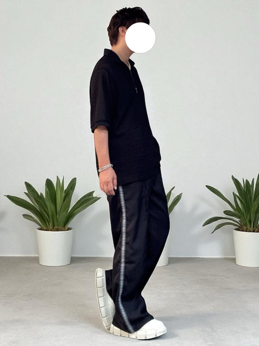 ブラック系のスラックス、ブラック系のポロシャツ、ホワイト系のスニーカーを着用したメンズの夏コーディネートの2枚目の写真