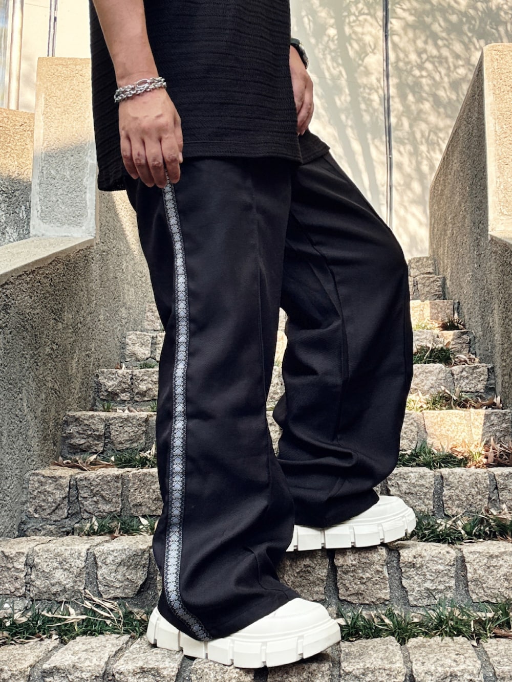 ブラック系のスラックス、ブラック系のポロシャツ、ホワイト系のスニーカーを着用したメンズの夏コーディネートの5枚目の写真