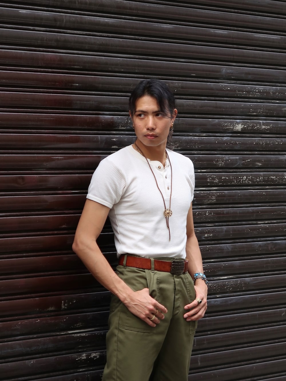 グリーン系のスラックス、ブラウン系のブーツ、ホワイト系のTシャツ/カットソーを着用したメンズの夏コーディネートの2枚目の写真