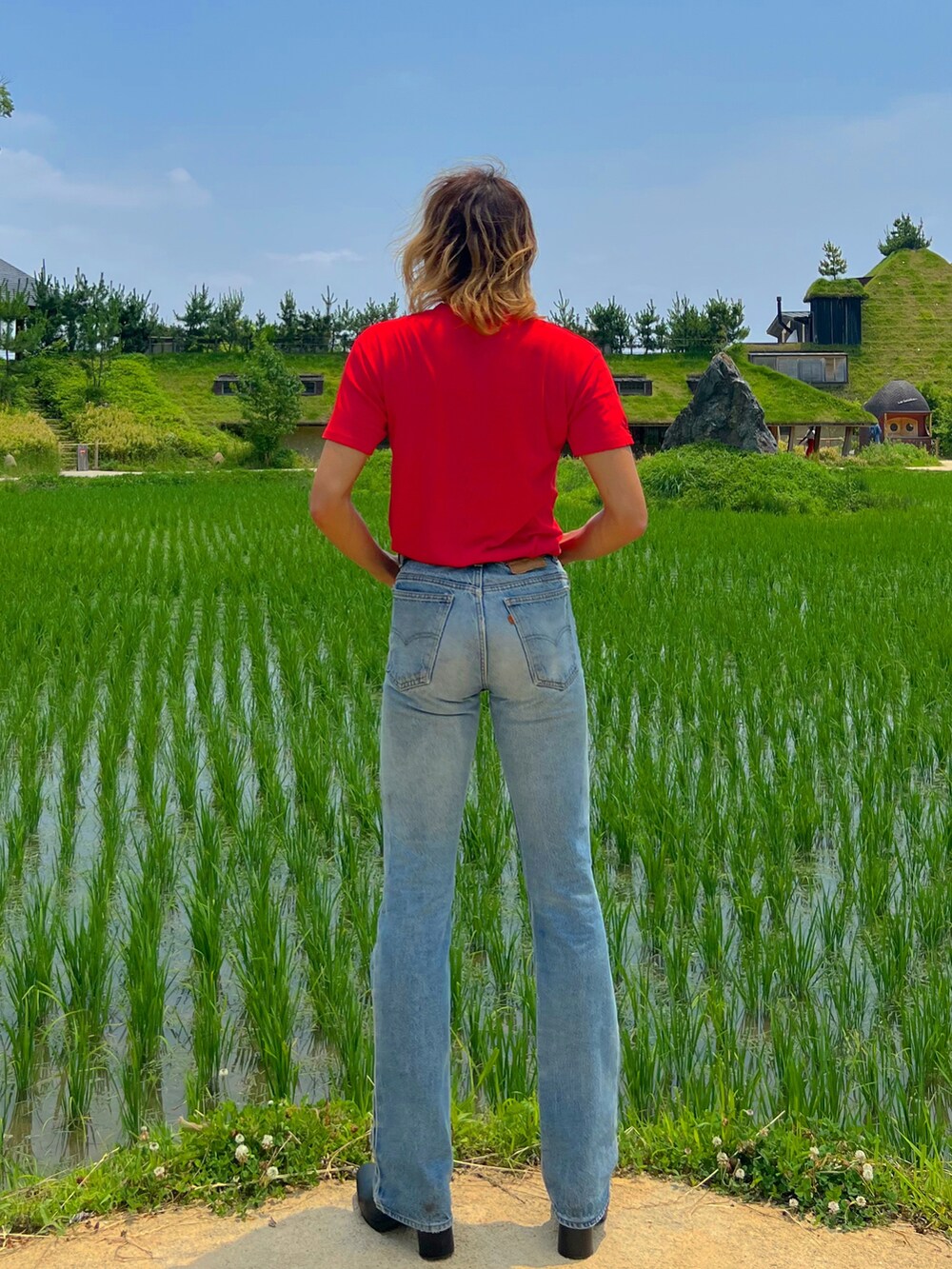 ブルー系のデニムパンツ、レッド系のTシャツ/カットソー、ブラック系のブーツを着用したメンズの夏コーディネートの2枚目の写真