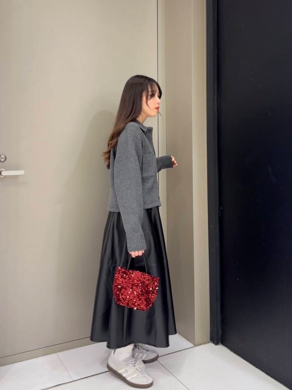 レッド系のショルダーバッグ、ブラック系のスカート、グレー系のニット/セーターを着用したレディースの秋コーディネートの2枚目の写真