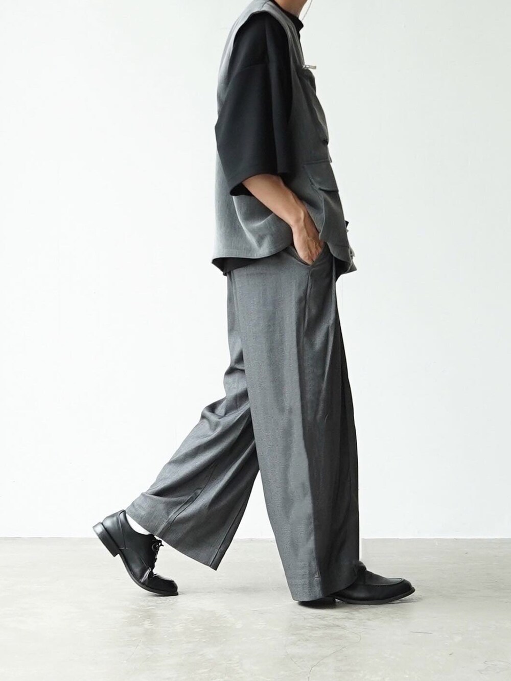 グレー系のベスト、ブラック系のTシャツ/カットソー、グレー系のスラックスを着用したメンズの夏コーディネートの2枚目の写真