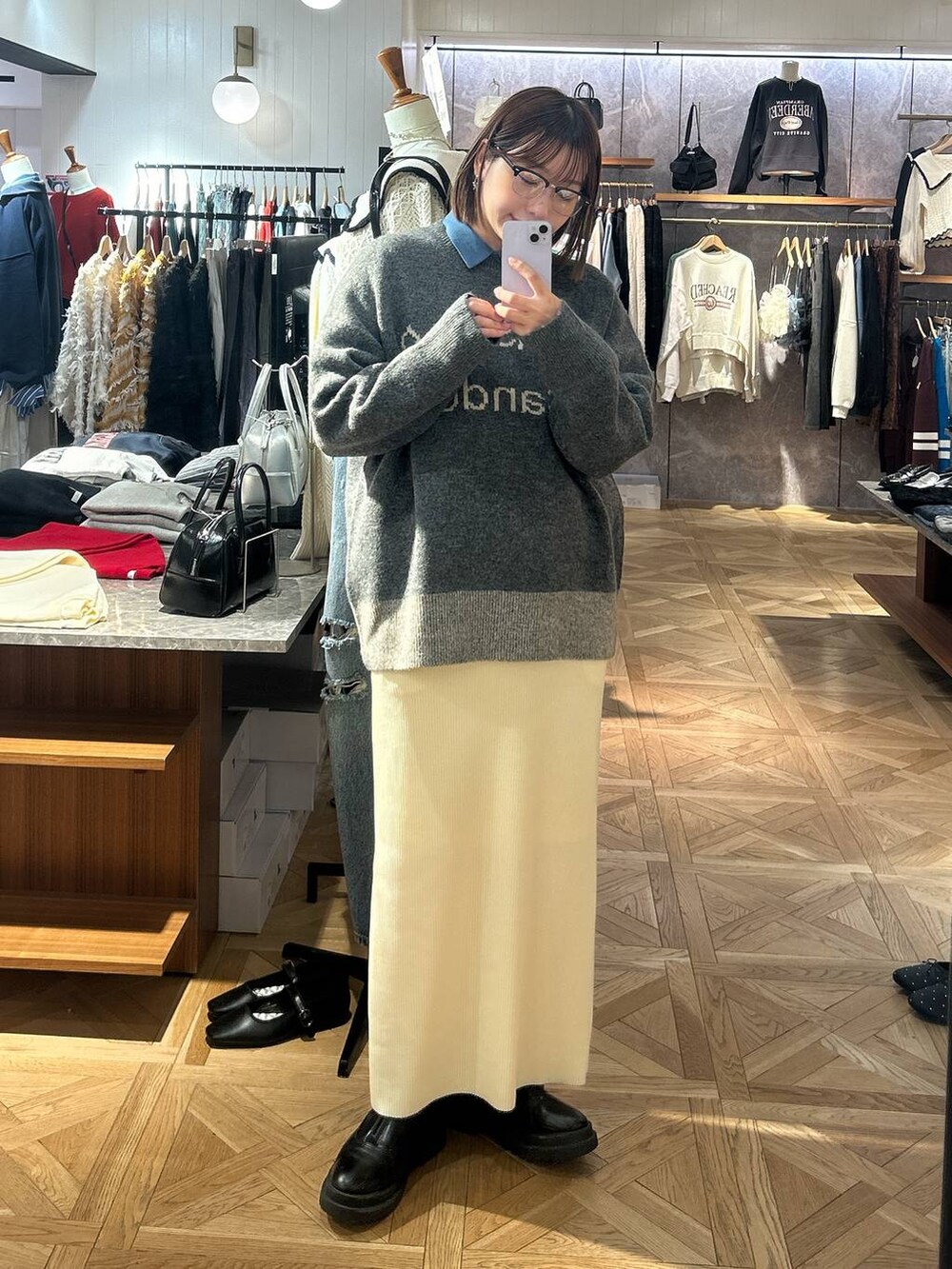 グレー系のスカート、グレー系のニット/セーター、ブルー系のシャツ/ブラウスを着用したレディースの秋コーディネートの2枚目の写真