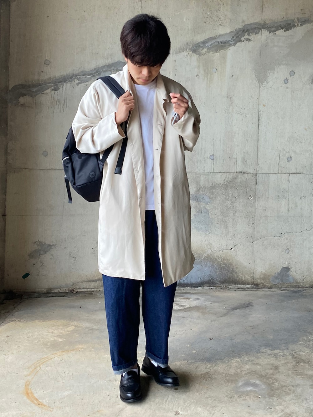 ベージュ系のステンカラーコート、ホワイト系のTシャツ/カットソー、ブルー系のデニムパンツを着用したメンズの秋コーディネートの2枚目の写真