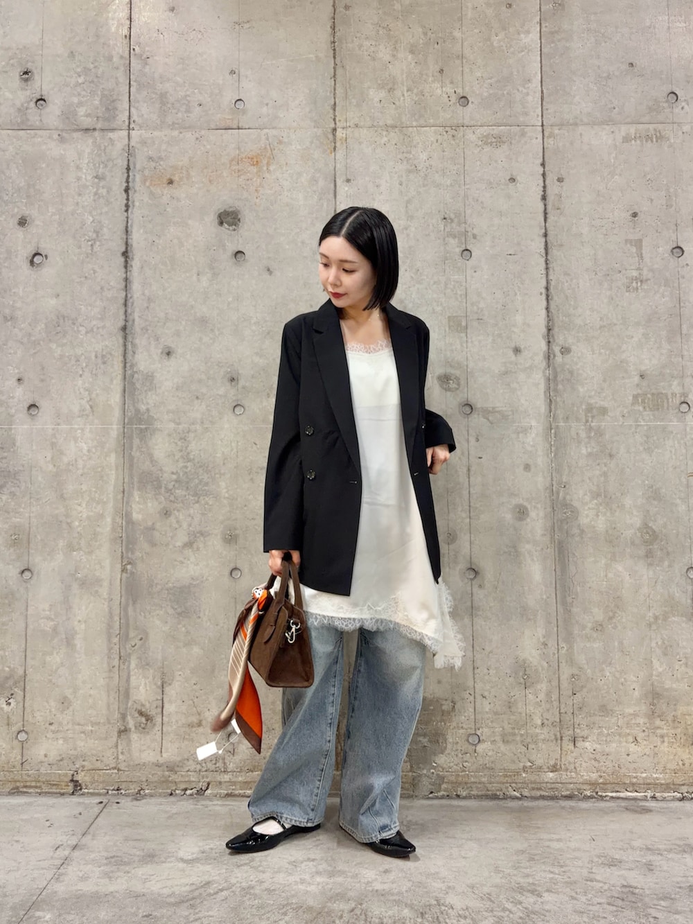 ブラック系のテーラードジャケット、ホワイト系のキャミソール、ブルー系のデニムパンツを着用したレディースの春コーディネートの2枚目の写真