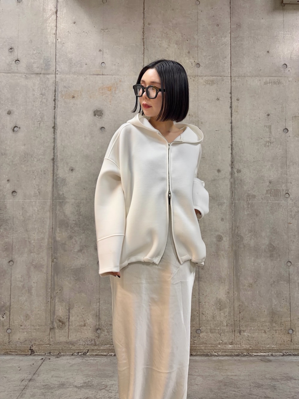 ホワイト系のパーカー、ホワイト系のスカート、ブラック系のメガネを着用したレディースの冬コーディネートの2枚目の写真