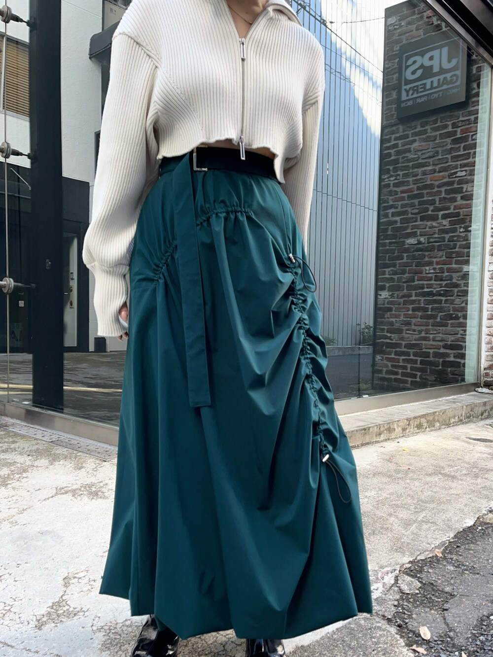 グリーン系のスカート、ホワイト系のニット/セーターを着用したレディースの冬コーディネートの4枚目の写真