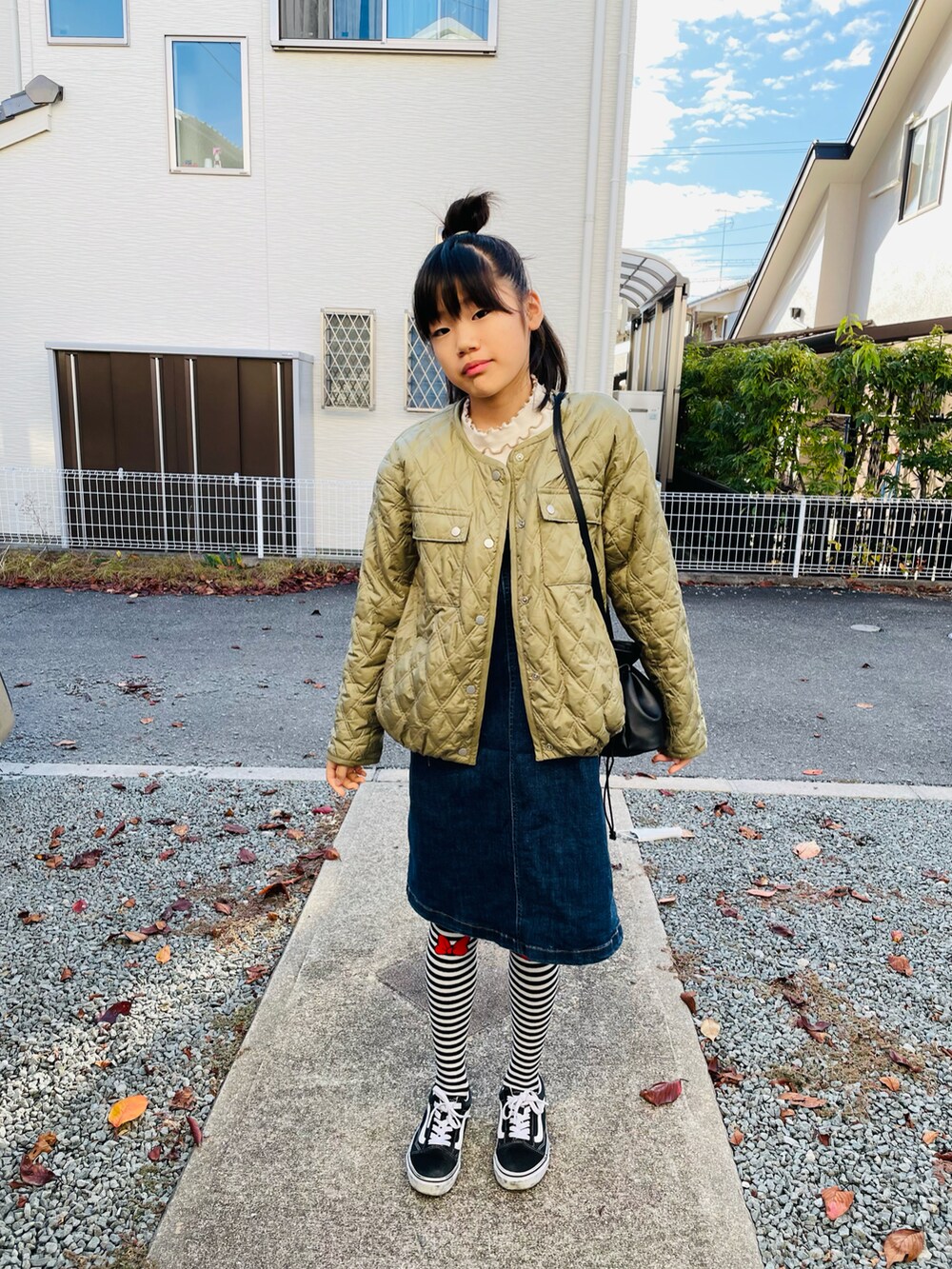 グリーン系のブルゾン、ブルー系のスカート、ブラック系のスニーカーを着用したキッズの秋コーディネートの2枚目の写真