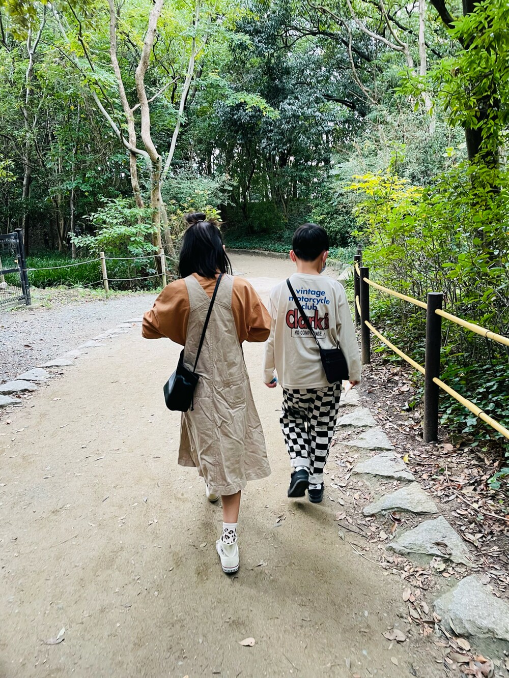 ブラック系のハンドバッグ、ベージュ系のジャンパースカート、ホワイト系のスニーカーを着用したキッズの秋コーディネートの2枚目の写真