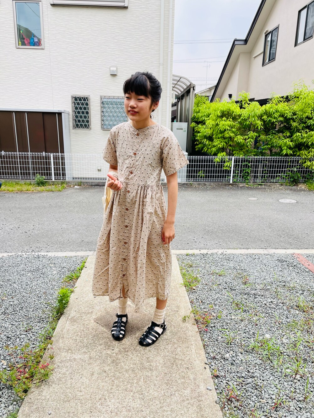 ベージュ系のシャツワンピース、ホワイト系のエコバッグ/サブバッグ、ブラック系のサンダルを着用したキッズの春コーディネートの2枚目の写真