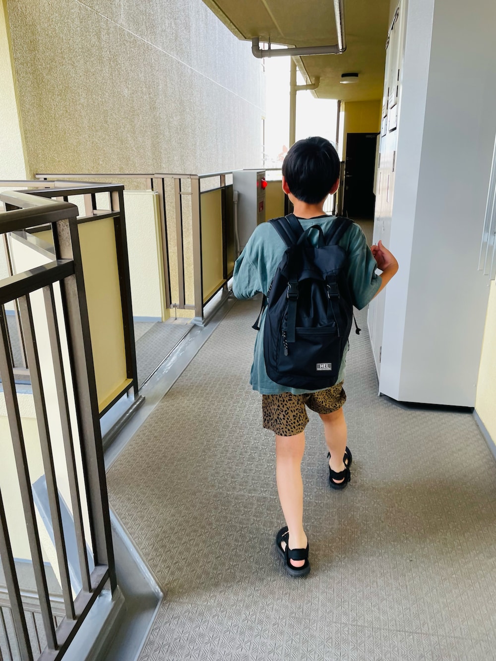 ブラック系のバックパック/リュック、グリーン系のTシャツ/カットソー、ブラック系のサンダルを着用したキッズの秋コーディネートの2枚目の写真