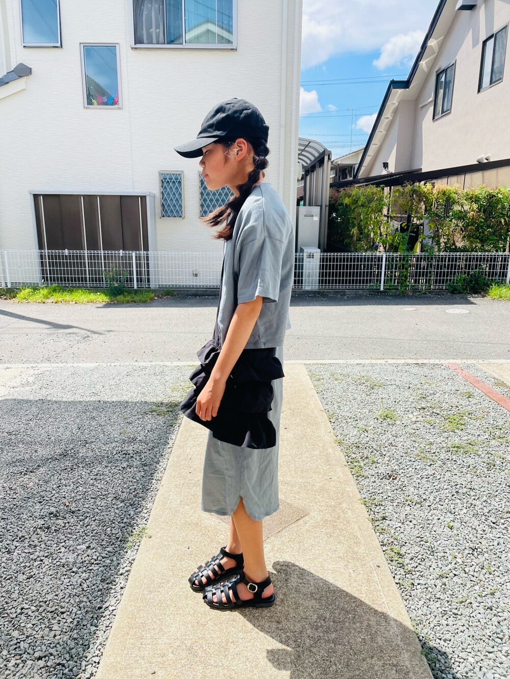 グリーン系のワンピース、ブラック系のサンダル、ブラック系のキャップを着用したキッズの夏コーディネートの2枚目の写真