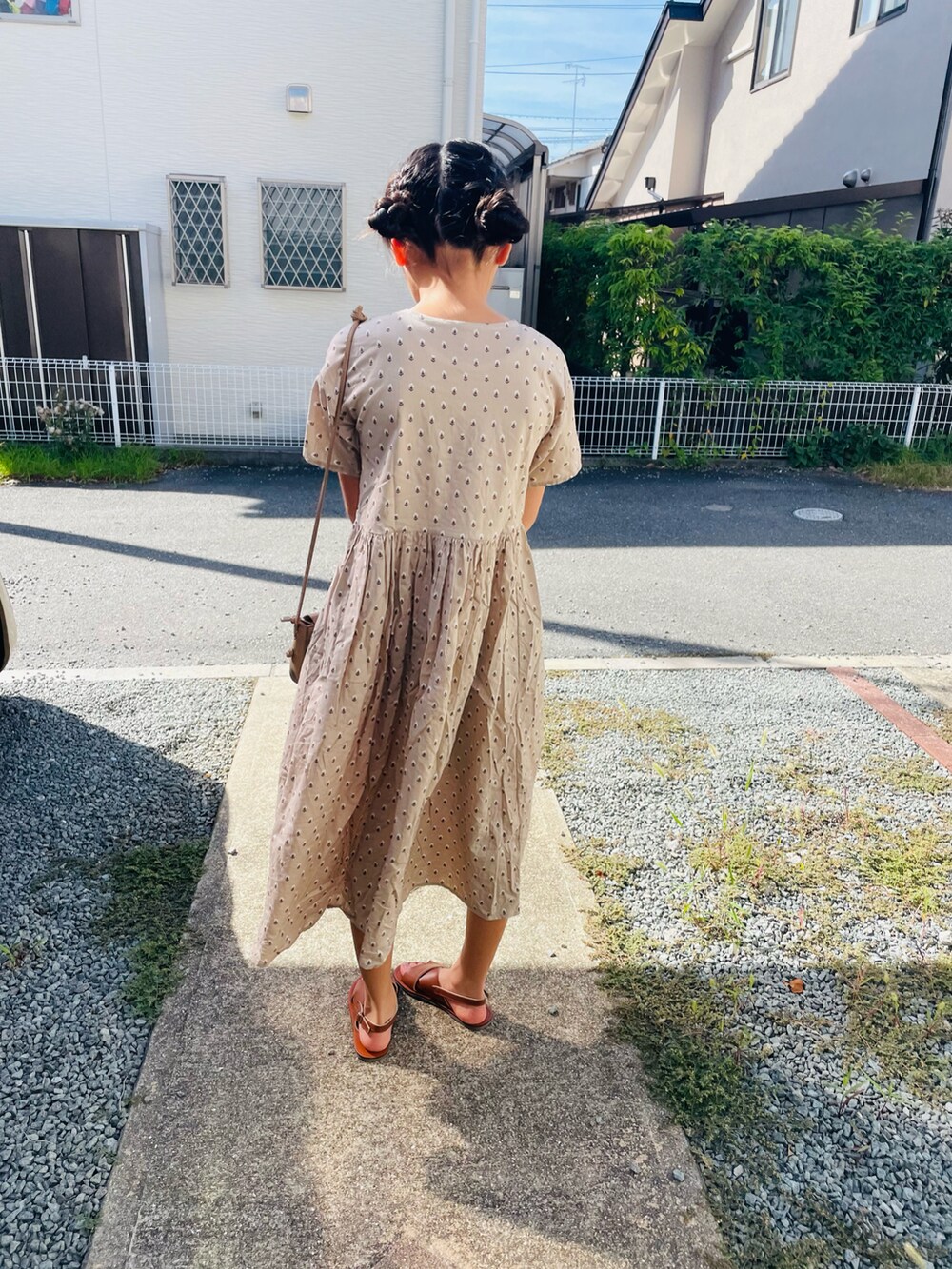 ベージュ系のシャツワンピース、ブラウン系のサンダル、ベージュ系のショルダーバッグを着用したキッズの夏コーディネートの3枚目の写真