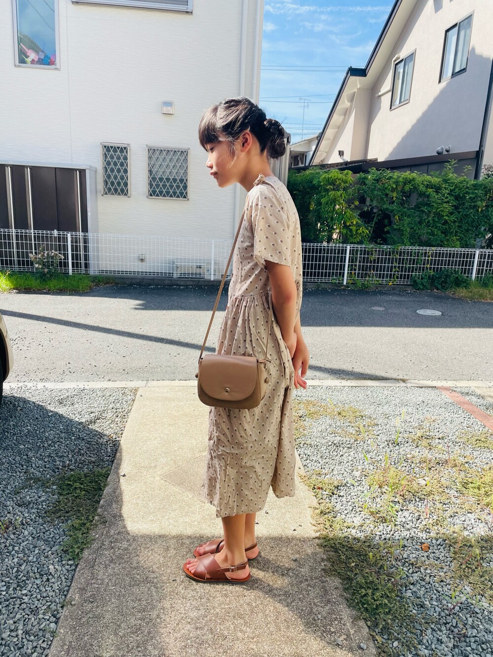 ベージュ系のシャツワンピース、ブラウン系のサンダル、ベージュ系のショルダーバッグを着用したキッズの夏コーディネートの2枚目の写真