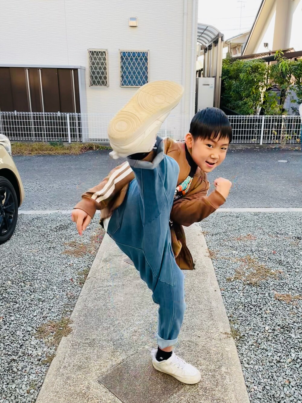 ブラウン系のノーカラージャケット、ブルー系のデニムパンツ、ホワイト系のスニーカーを着用したキッズの秋コーディネートの4枚目の写真