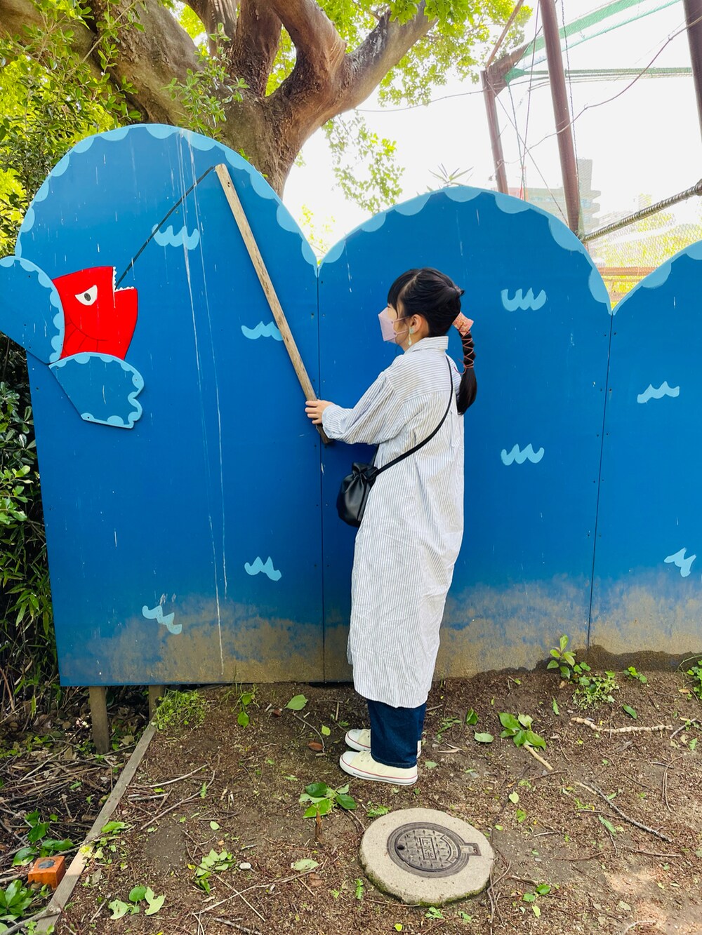 ブルー系のシャツワンピース、ブラック系のハンドバッグ、ブルー系のデニムパンツを着用したキッズの春コーディネートの3枚目の写真