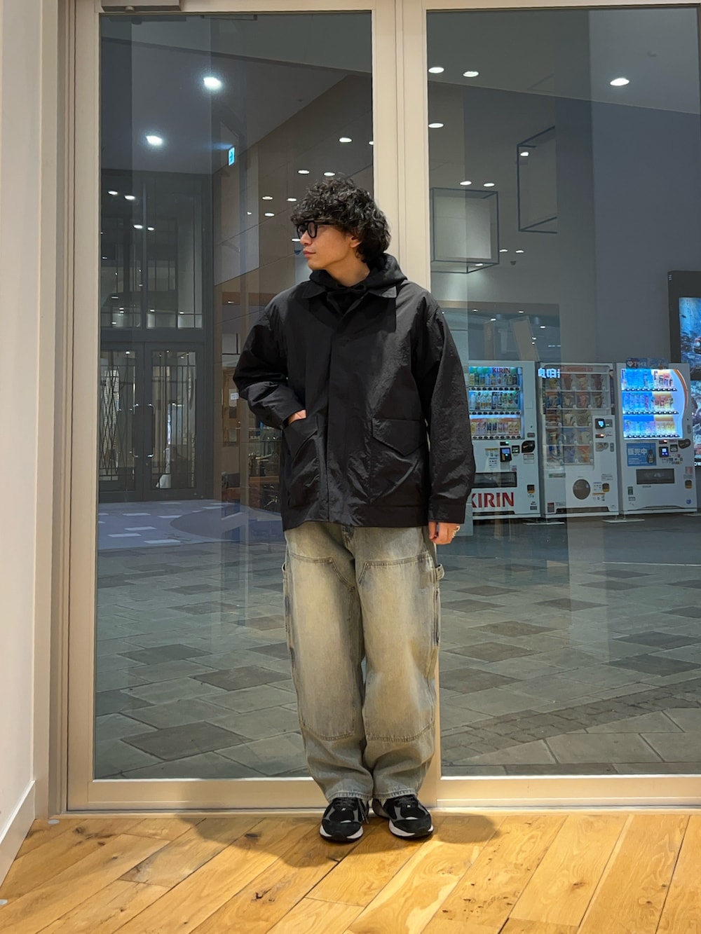 ブラック系のナイロンジャケット、ブラック系のパーカー、ブルー系のデニムパンツを着用したメンズの春コーディネートの3枚目の写真
