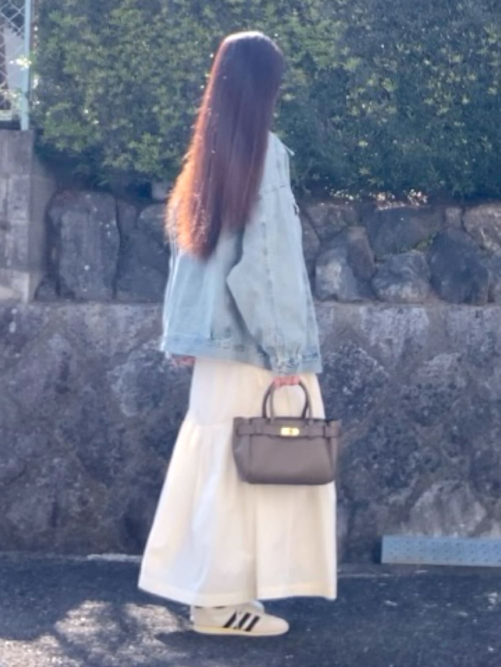 ブルー系のデニムジャケット、ベージュ系のハンドバッグ、ブラック系のニット/セーターを着用したレディースの春コーディネートの2枚目の写真