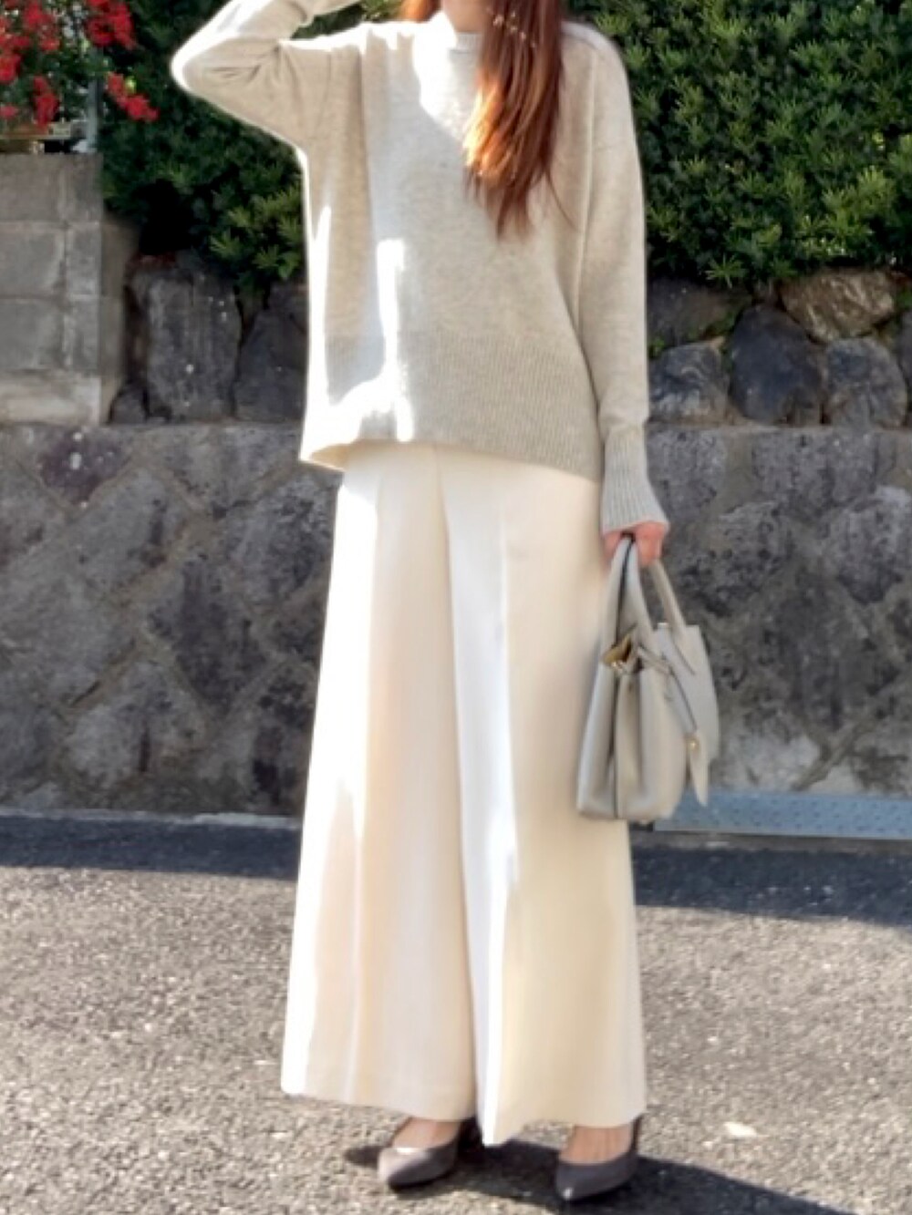 グレー系のニット/セーター、グレー系のハンドバッグ、ホワイト系のパンツを着用したレディースの秋コーディネートの2枚目の写真