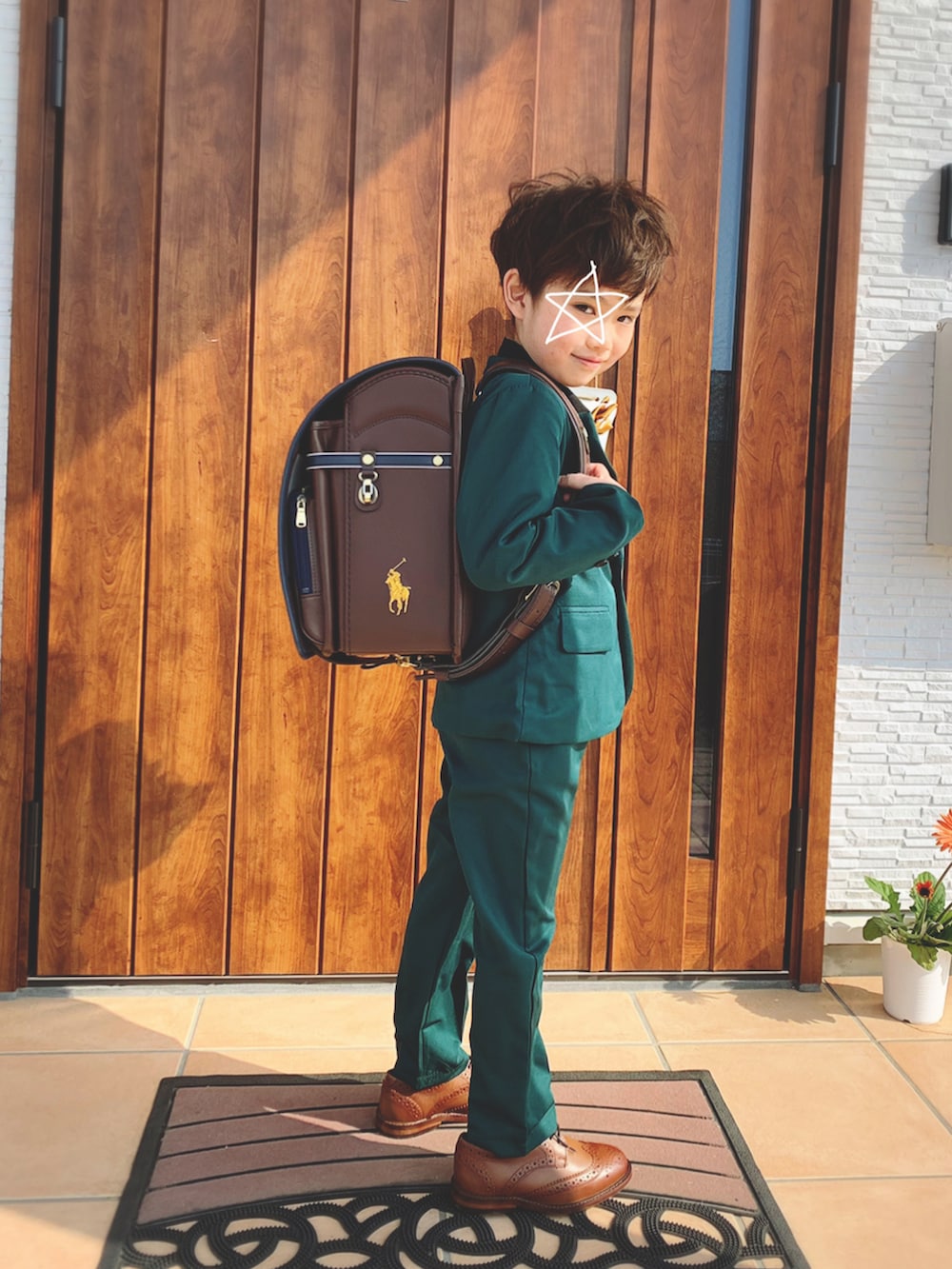 グリーン系のスーツセット、ブラウン系のドレスシューズ、ブラウン系のランドセルを着用したキッズの春コーディネートの2枚目の写真